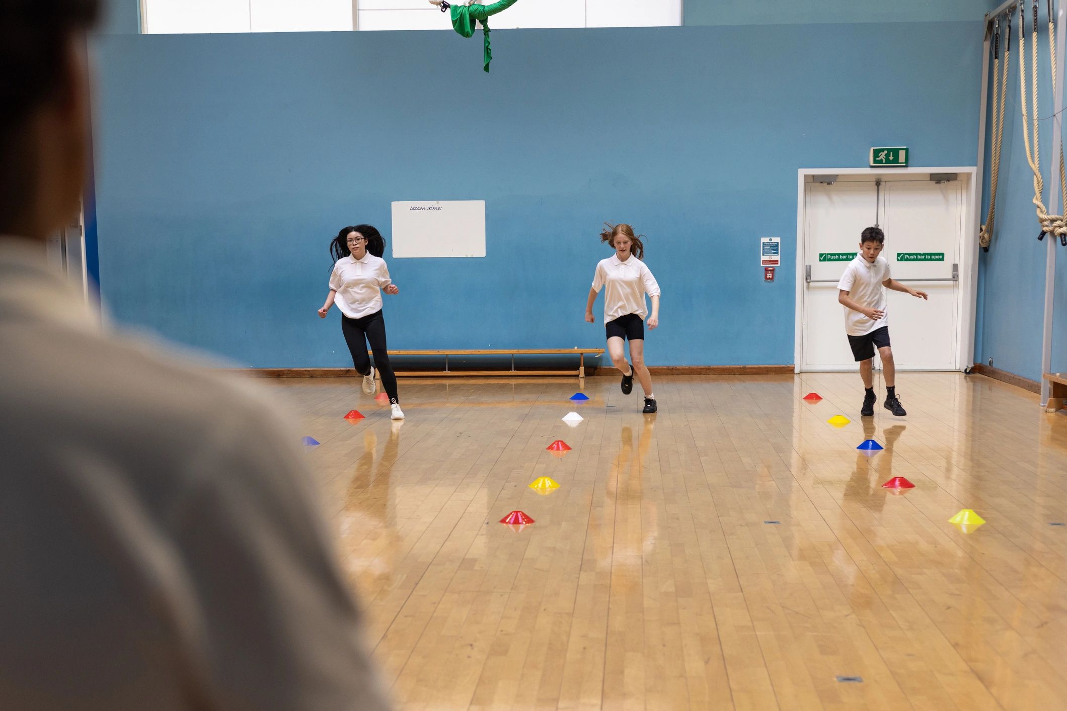 Youth athletes running a conditioning drill with cones on a gym floor